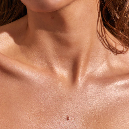 This image showcases a close-up of a person’s collarbone and neck area, displaying a sun-kissed glow and radiant skin. The effect highlights the use of Summer Skin gradual tanning lotion, providing a natural, even tan with a luminous finish.